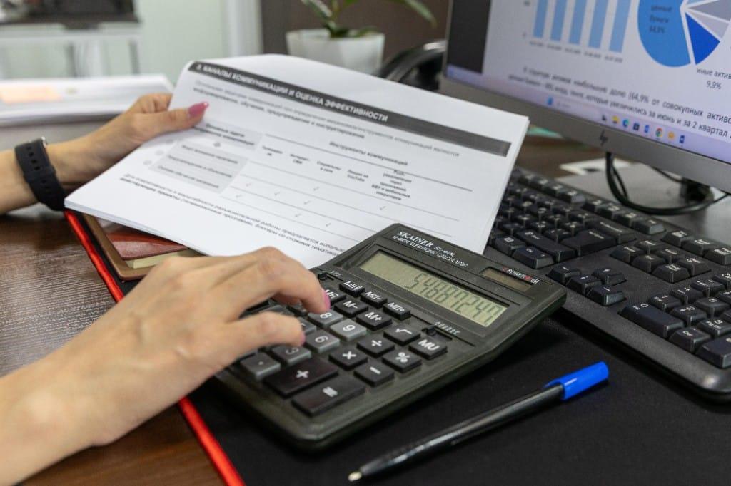 Analyst reviewing financial schedules and calculating figures beside a computer showing charts, illustrating valuation work in a dispute